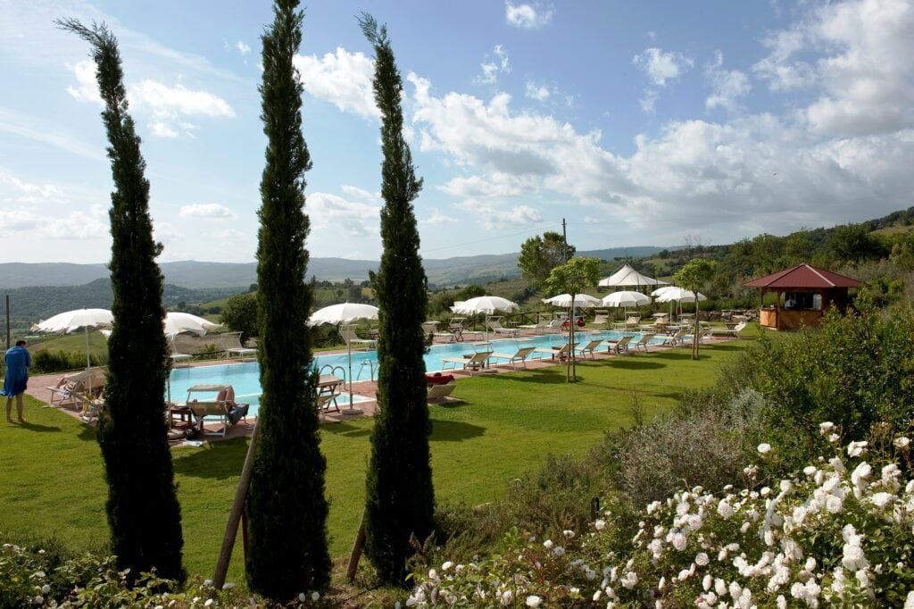 Vista di una piscina all'aperto circondata da giardini e ombrelloni.