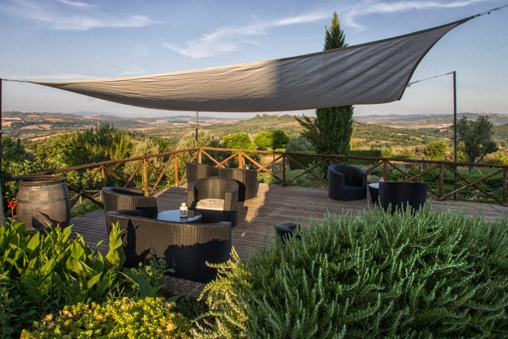 Terrazza arredata con sedie e tavoli sotto una copertura, con vista panoramica su colline verdi.